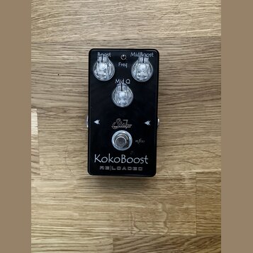 Černý kytarový efekt s nápisem KokoBoost RELOADED a logem Suhr. Na horní straně jsou tři ovládací knoflíky s popisky Boost, Freq a MidBoost (u prostř…