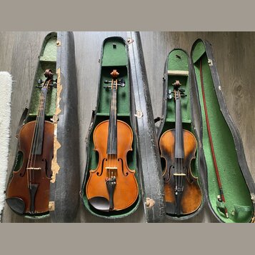 Tři hnědé housle v otevřených černých pouzdrech s zeleným vnitřkem. Vedle nich leží jeden smyčec s červeným dřevěným hřádem. Na nástrojích nejsou vid…
