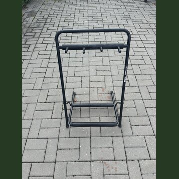 Černý kovový stojan na hudební nástroje s horní lištou vybavenou čtyřmi kolíky. Na pravém bočním sloupeku je viditelný bílý nápis th.mann. Povrch sto…