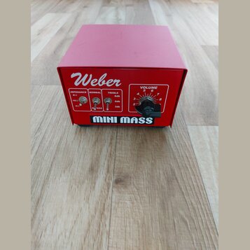 Červený hranatý přístroj s nápisem Weber a MINI MASS. Na přední straně jsou přepínače označené jako IMPEDANCE (8Ω, 16Ω, 4Ω), NORMAL a TREBLE (6db, 0d…