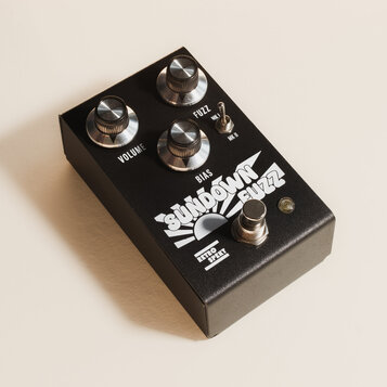 Černý efekt pedál s nápisy VOLUME, FUZZ a BIAS. Na spodní části je bílý grafický symbol slunce a nápis SUNDOWN FUZZ s malým logem RETRO SPRINT. Zaříz…