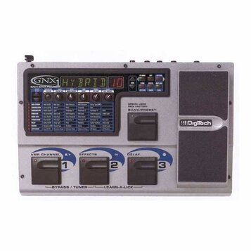 Šedý kytarový procesor s nápisem GNX1 GuitarFx GUITAR PROCESSOR. Displej zobrazuje text HYBRID 10 a vedle jsou umístěny ovládací tlačítka a potenciom…