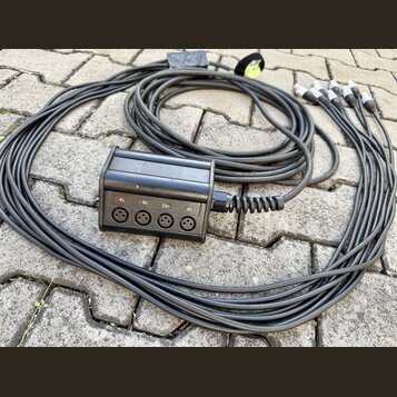 Černý rozbočovací kabel s plastovým rozdělovačem. Na přední straně rozdělovače jsou čtyři konektory XLR a nad nimi nápisy 01., 02., 03. a 04. Kabel j…