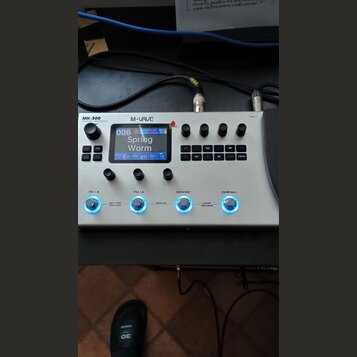 Bíle provedený multifunkční efektový procesor s nápisem MK-300 a logem M-VAVE. Zařízení má digitální displej, na kterém je zobrazen text 006 Spring W…