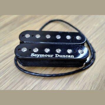 Černý humbucker s dvěma řadami magnetických pólů. Na spodním snímači je bílý nápis Seymour Duncan. Povrch plastového krytu vykazuje drobné škrábance…