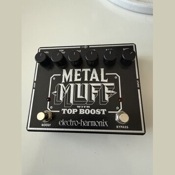 Černý efekt pedál s bílými nápisy. Na horní části jsou šest ovládacích knoflíků s popisky VOL, TOP BOOST, MIDDLE, BASS a DIST. Uprostřed je velký náp…