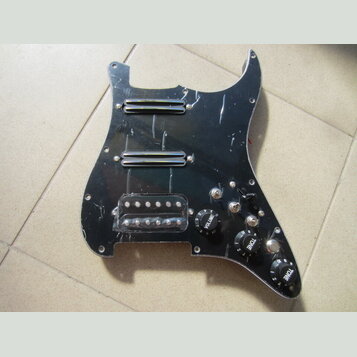 Černý plastový pickguard pro elektrickou kytaru s třмя snímači. Horní dva jsou humbuckery s chromovaným krytem, spodní je singl v průhledném plastové…
