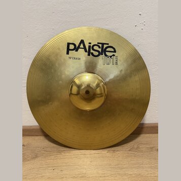 Zlatý mosazný činel s koncentrickými drážkami na povrchu. Na horní části je černý nápis pAiste, pod ním text 16" CRASH a vedle něj označení 101 BRASS…