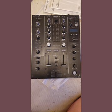 Černý dvoukanálový DJ mixér s nápisem Pioneer DJ v horní části. Na spodním pravém rohu je uveden model 2 CHANNEL DJ MIXER DJM-450. Přístroj obsahuje…