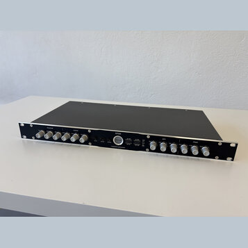 Černý rackový procesor s nápisem xmax a masterbus processor. Uprostřed je kulaté logo s textem Elysia. Zařízení má v horní části řadu stříbrných otoč…