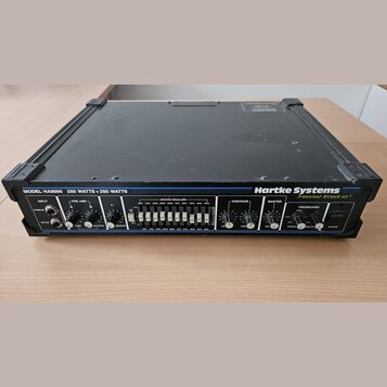 Černý rackový zesilovač s nápisy MODEL: HA5000 a 250 WATTS + 250 WATTS. Na pravé straně je bílé logo Hartke Systems a pod ním nápis Transient Attack.…