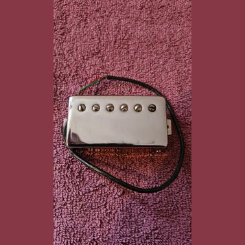 Stříbrný humbucker s chromovaným krytem a šesti viditelnými šrouby. Z nástroje vedou červený, zelený a černý vodič. Povrch krytu vykazuje drobné škrá…