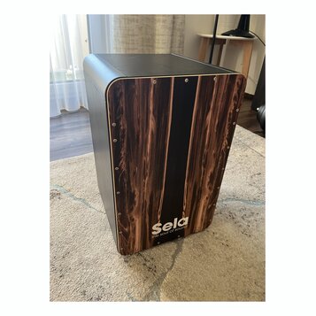 Černý cajon s přední deskou v imitaci tmavého dřeva. Ve spodní části je bílý nápis Sela a pod ním menší text the soul of sound. Povrch je hladký, v r…