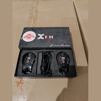 Černý bezdrátový systém pro kytaru v originálním černém kartonovém boxu. Na krabici je bílé logo Xvive, nápis Wireless Guitar System a červenobílá ná…