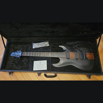 Černá elektrická kytara v otevřeném černém kufru. Na hlavě je logo CHAPMAN GUITARS a na hrazence symbol nekonečna. Tělo kytary je matně černé s vidit…