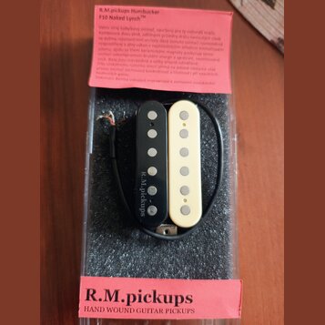 V plastovém obalu na černém molitanu jsou dva kytarové snímače typu humbucker, jeden v černé a druhý v krémové barvě. Na černém snímači je svisle nap…