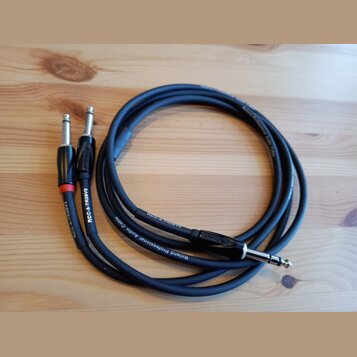 Černý audio kabel s konektory typu jack. Na kabelu je v bílém tisku nápis Roland Professional Audio Cable a označení RCC-5-TR28V2. Na jednom z konekt…