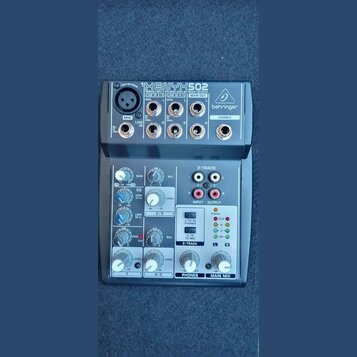 Šedý mixážní pult značky behringer s označením XENYX 502. Na horní části jsou vstupy MIC, LINE IN a výstupy MAIN OUT a PHONES. Spodní panel obsahuje…