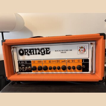 Kytarový zesilovač v oranžovém texturovaném potahu s bílým předním panelem. Na panelu je velký nápis ORANGE a modelové označení ROCKERVERB 100 MKIII…