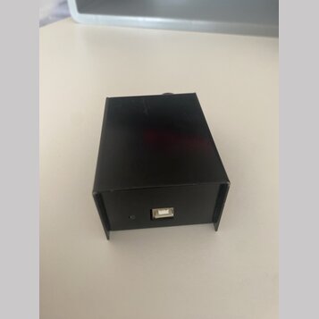 Černý obdélníkový box z kovového nebo plastového materiálu. Na přední straně je umístěn jeden USB port a malá čtvercová kontrolka. Povrch je hladký a…