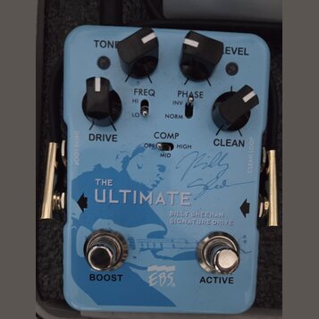 Modře barevný efekt pedál s nápisy THE ULTIMATE a BILLY SHEEHAN SIGNATURE DRIVE. Na spodní části je logo EBS a dva stomečové spínače s popisky BOOST…