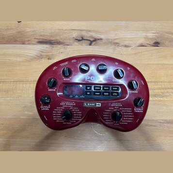 Červený kytarový procesor značky LINE 6. Na horní části jsou ovládací knoflíky s popisky DRIVE, BASS, CHANNEL a REVERB, uprostřed je nápis POD. Spodn…