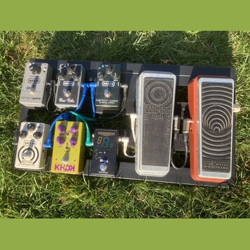 Kytarový efektový pedalboard s osmi pedály umístěnými na černé desce. V horní řadě jsou pedály MXR smartgate, MXR Uni-Vibe. a MXR carbon copy analog…