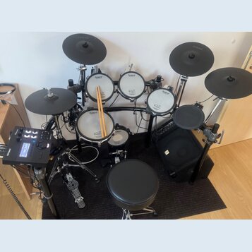 Elektronická bicí souprava značky Roland v černé barvě s bílými bubny. Na bubnech je viditelné logo Roland a nápis V-Drums. Součástí sady je ovládací…
