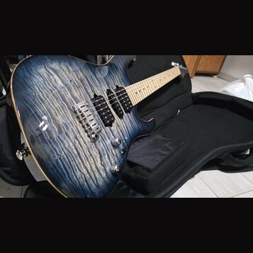 Elektrická kytara s modrým plamenovitým povrchem těla a světlým hnedým hmatníkem. Nástroj má tři humbuckery, chromovaný most a dva ovládací knoflíky.…