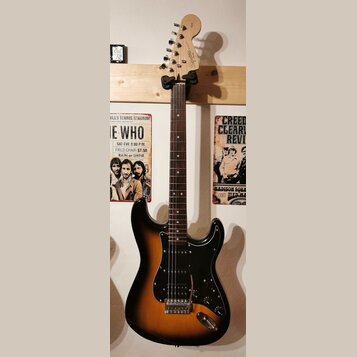 Elektrická kytara s trupem v barevnosti sunburst a černým pickguardem. Na hlavě hmatníku je nápis "Squier STRAT". Nástroj má hmatník z tmavého dřeva…
