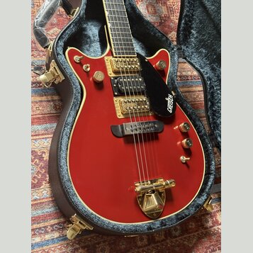 Červená elektrická kytara s gold hardwarem v černém tvrdém kufru. Na černé plechovce je bílý nápis GRETSCH. Nástroj má dva snímače, zlaté knoflíky a…
