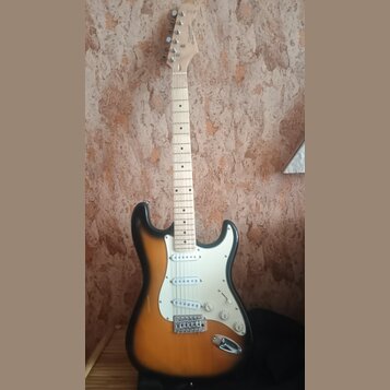 Elektrická kytara s tělem v žlutě-černé barvě (sunburst) a bílým pickguardem. Na hlavě hnedku je viditelné logo Squier. Hmatník je vyroben ze světléh…