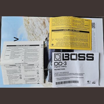 Fotografie zobrazuje papírový návod k obsluze efekt pedálu. Na bílém podkladu je výrazné černé logo BOSS a název modelu DD-3 Digital Delay. Text obsa…