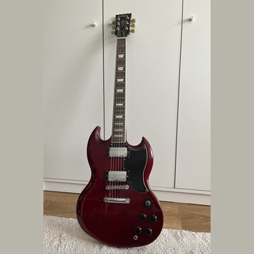 Kytara s tmavě červeným lakem a černým pickguardem. Na hlavě je viditelné zlaté logo Epiphone. Nástroj má dva humbuckery, tři ovládací knoflíky a pře…