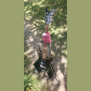 Černá elektrická kytara s výrazným, ostře hranatým tvarem těla a hlavy. Na hlavě je bílý nápis B C Rich. Kytara má dva humbuckery, hnedový hmatník a…