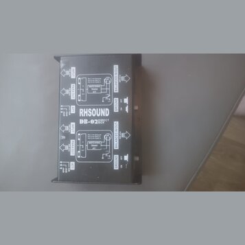 Fotografie zachycuje zadní stranu černé DI boxy s bílým technickým popisem. Na zařízení je uveden nápis RH SOUND DB-02 DIRECT BOX. Jsou zde viditelné…