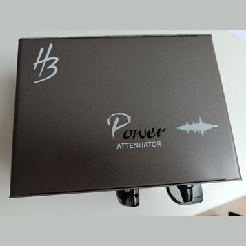 Černý kovový box s nápisem Power ATTENUATOR a grafickým symbolem zvukové vlny. V levém horním rohu je bílé logo znázornující stylizované písmeno H s…
