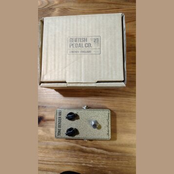Kartonová krabice s nápisem BRITISH PEDAL CO. LONDON - ENGLAND. Pod ní je efekt pedál v béžovém provedení s kovovým spínacím tlačítkem a dvěma černým…