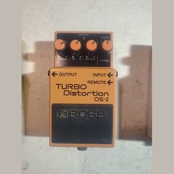 Oranžový efekt pedál s černým ovládacím panelem a černým spodním spínačem. Na zařízení jsou nápisy TURBO Distortion DS-2 a logo BOSS. Horní panel obs…