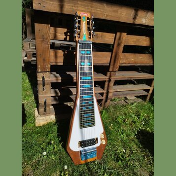 Elektrická lap steel kytara s dřevěným korpusem a bílým krycí plátem. Na hlavě je červený nápis Sondley a pod ním zelený nápis Steel Guitar. Hmatník…