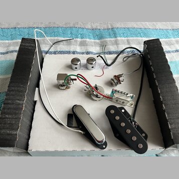 Sada elektroniky pro elektrickou kytaru rozmístěná na bílém podkladu. Soubor obsahuje dva chromované knofíky, jeden přepínač, potenciometr, vstupní j…