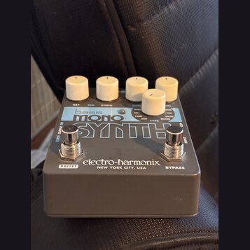 Šedý kytarový efekt s bílými oválnými knoflíky. Na horní straně je nápis bass MONO SYNTH a v dolní části značka electro-harmonix NEW YORK CITY, USA.…