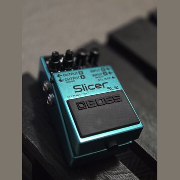 Modrý kytarový efekt pedál s černým nášlapným spínáčem. Na horní straně je bílý nápis Slicer SL-2 a pod ním text SET TEMPO/HOLD. Na spínáči je vyraže…