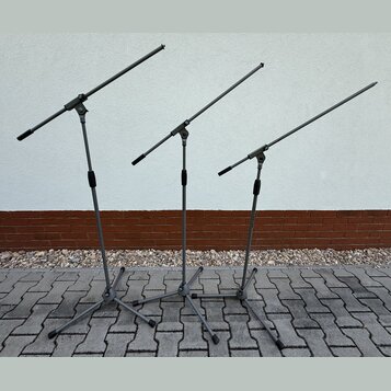 Tři šedé mikrofonní stojany s rameny. Stojany mají trojnožku a teleskopické části s černými utahovacími knoflíky. Povrch je matný, bez viditelných zn…