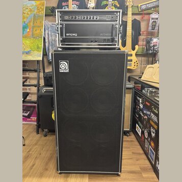 Sada basového zesilovače a reproduktorové skříně v černé barvě. Horní část obsahuje rack s nápisy SVPCL a ampeg SVT-300. Spodní reproduktorová skříně…