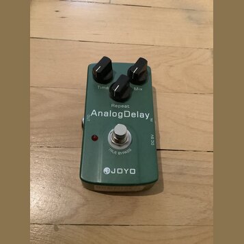 Zelený efekt pedál s nápisy AnalogDelay, JOYO a TRUE BYPASS. Na horní části jsou dva černé ovládací knoflíky s popisky Time a Mix, mezi nimi je nápis…