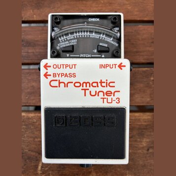 Bílý kytarový ladič značky BOSS, model TU-3 Chromatic Tuner. Horní část tvoří analogový displej s nápisy CHECK, -50, +50 a označením strun BASS a GUI…
