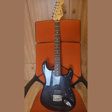 Černá elektrická kytara s tmelem v barvě přírodního dřeva. Na hlavě je viditelné logo Squier. Kytara má tři snímače, chromovaný most a ovládací knofl…