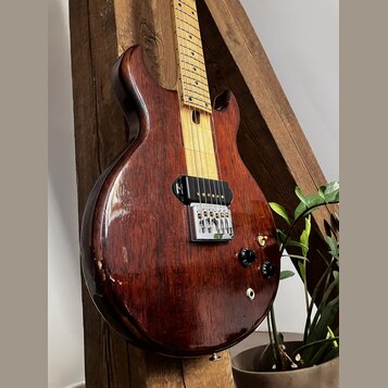 Elektrická kytara s tmavě hnědým dřevěným korpusem a světlým javorovým hmatníkem. Nástroj má jeden černý humbucker u kobylky, stříbrný strunník a dva…
