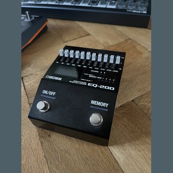 Černý grafický ekvalizér s bílými posuvníky a dvěma stomečními spínači. Na přístroji jsou nápisy BOSS, GRAPHIC EQUALIZER EQ-200, ON/OFF a MEMORY. Nad…